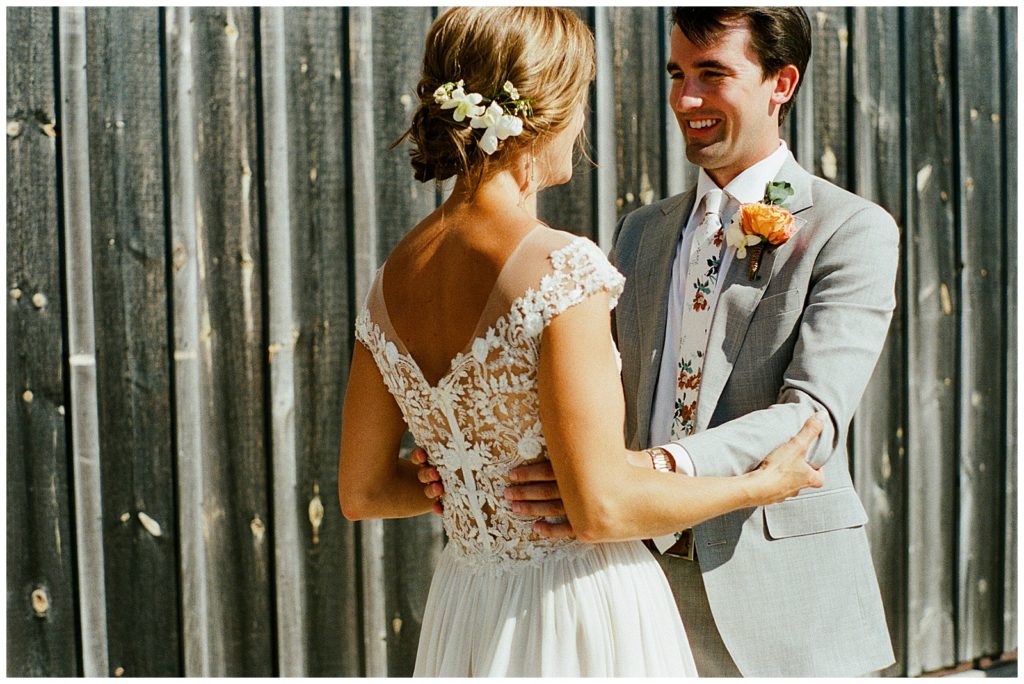 In wedding photography on film, a bride and groom dance outside a gray barn.