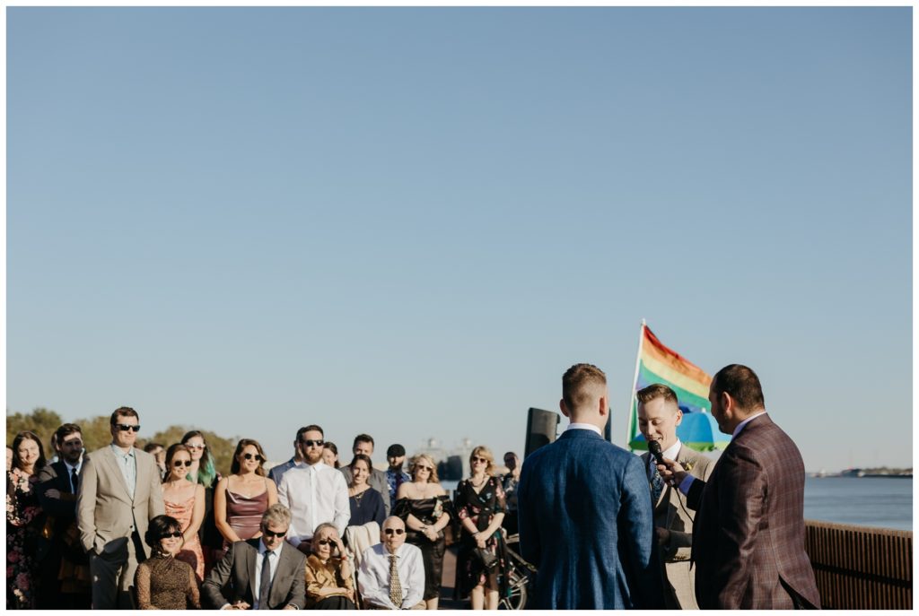 A photograph of the grooms looking at the officiant during the Tigermen Den wedding
