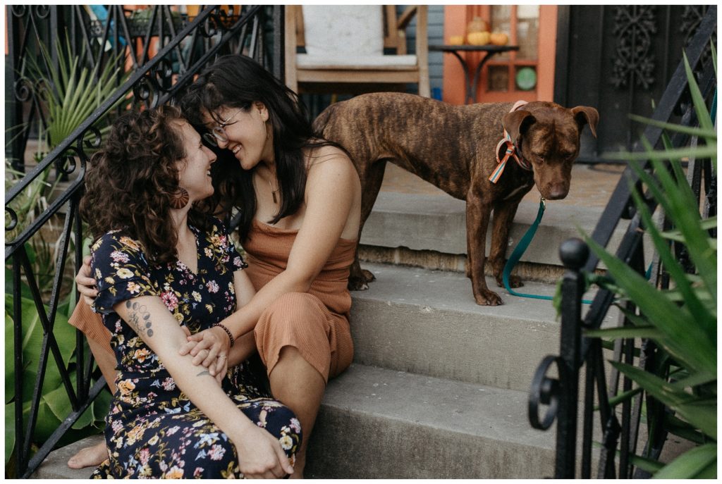 The couple's dog stands behind them in their engagement photos at home