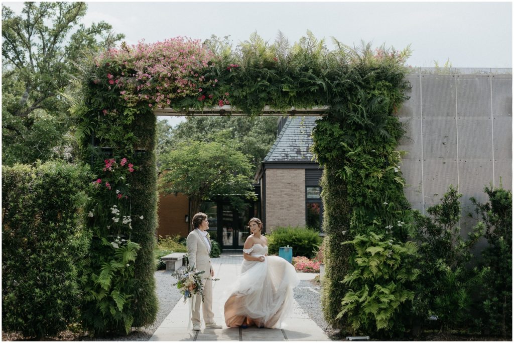 Britt twirls beside Em under a green and pink plant-covered archway at their New Orleans Botanical Garden wedding.