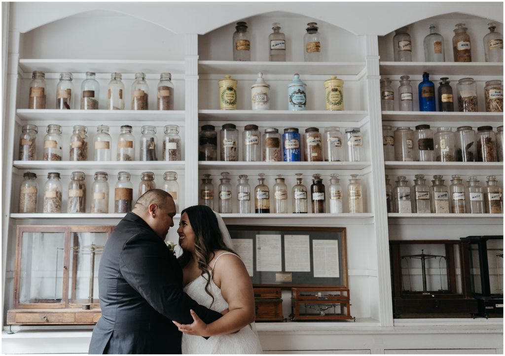 The couple stands in front of a wall of Pharmacy Museum antiques.