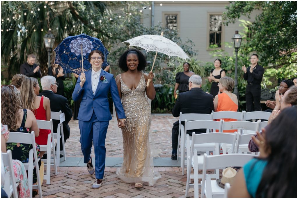 Alex and Isatu carry blue and white wedding umbrellas.