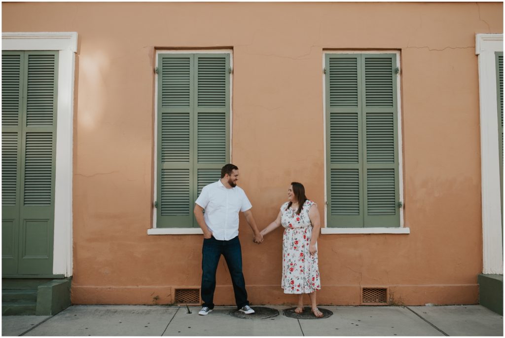 A couple holds hands in front of a peach French Quarter house.