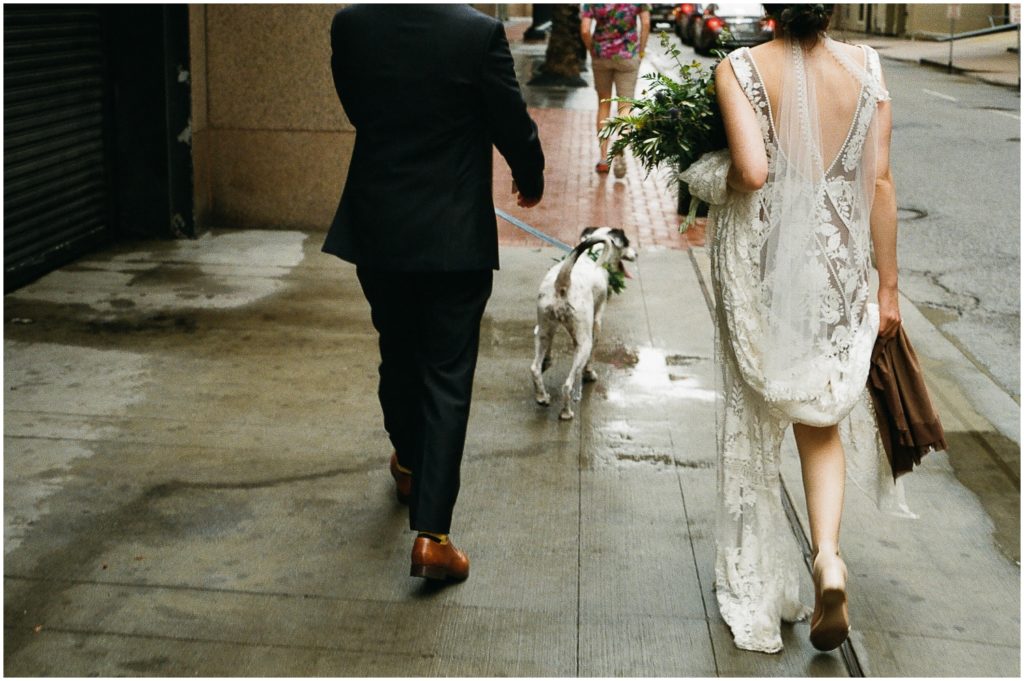 Marissa carries the train of her wedding dress as they walk down the wet New Orleans street.
