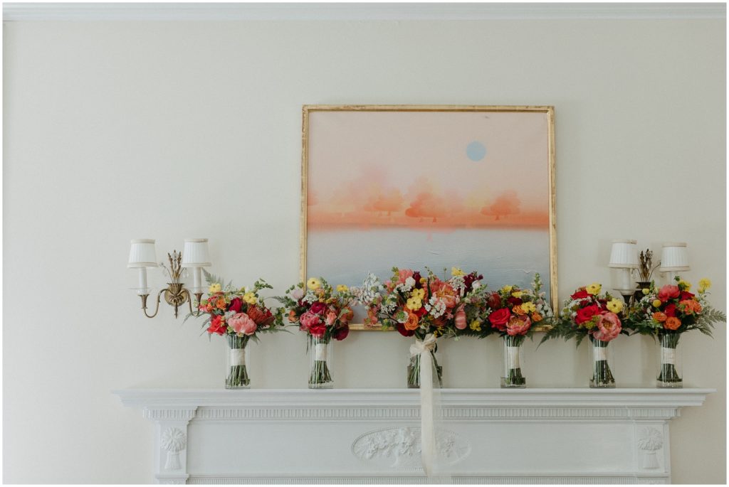 A line of wedding bouquets sits under a pink and orange painting.
