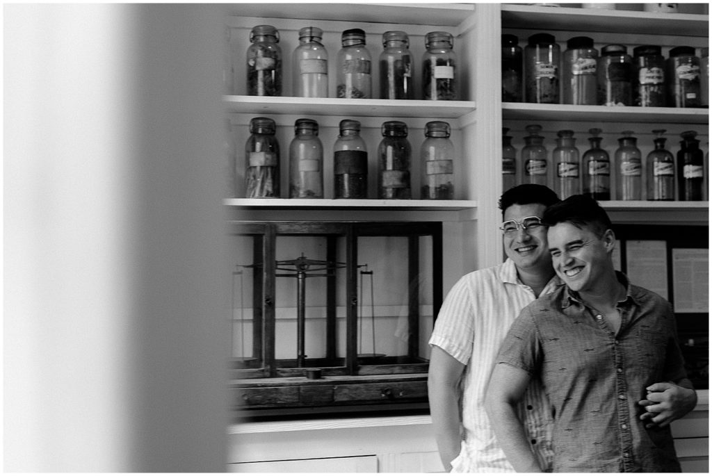 Caleb leans against Enrique at the Pharmacy Museum counter in French Quarter engagement photos.