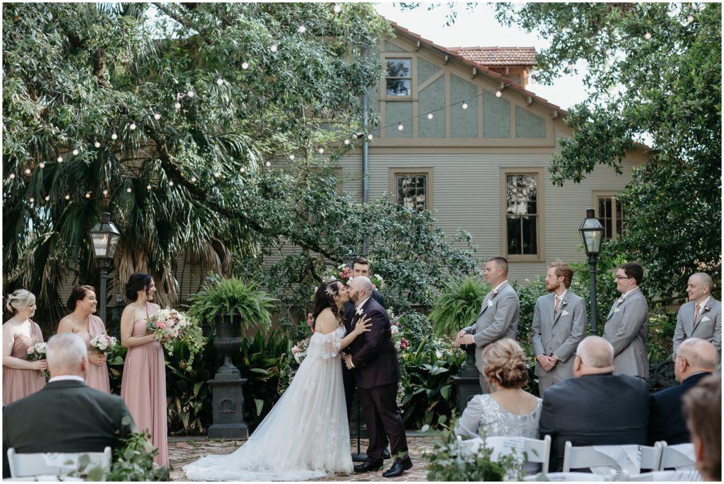 A couple kisses at the end of a courtyard wedding.