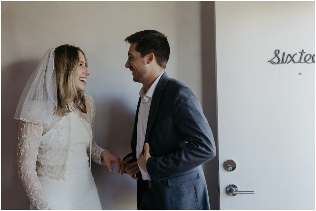A bride and groom laugh beside a Drifter Hotel door.