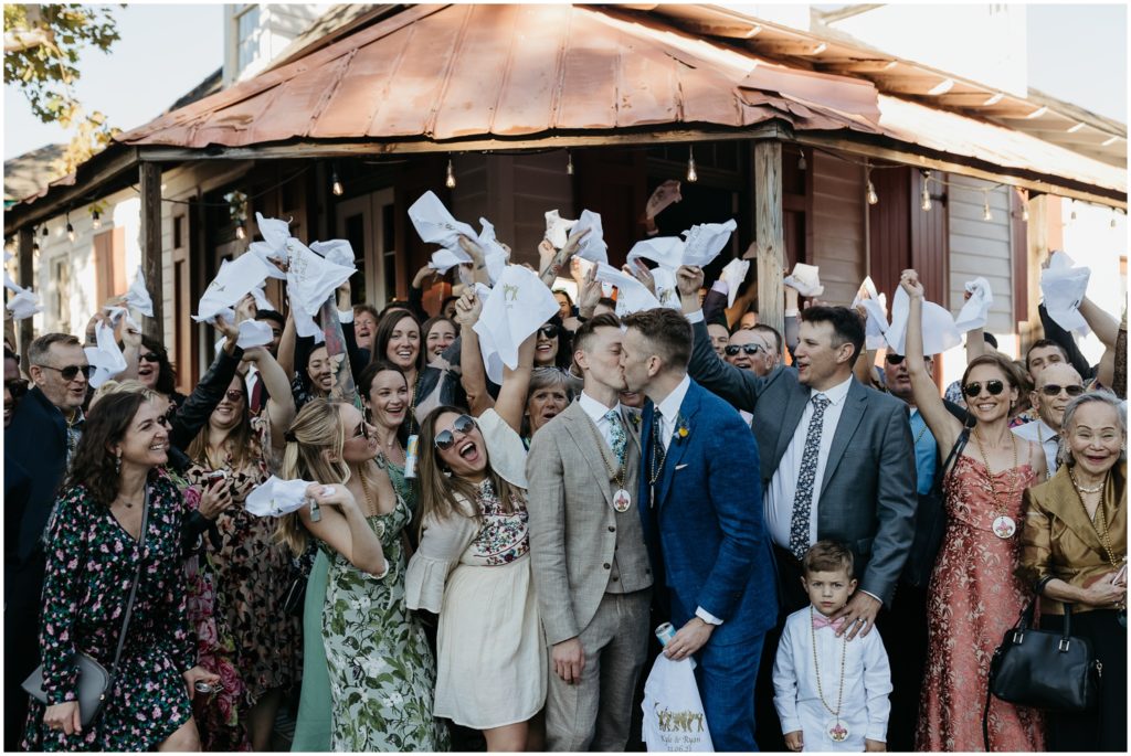 Two grooms kiss surrounded by wedding guests at their New Orleans destination wedding.