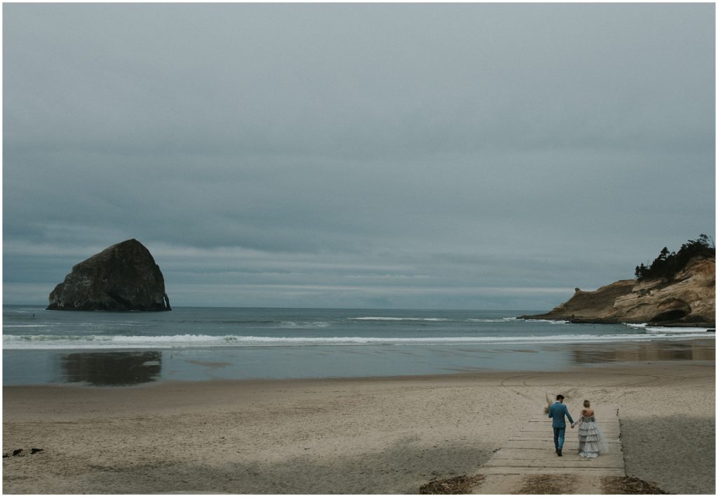 A wide angle shows a couple walking in the distance on the beach at Cape Kiwanda.