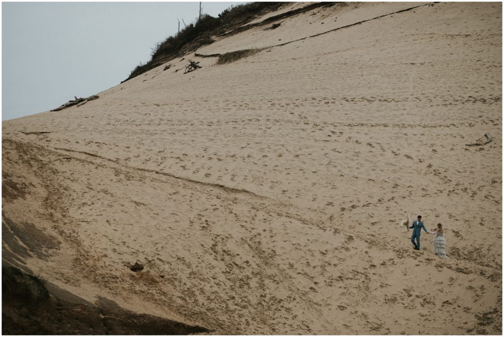 A couple walks over a large sand dune.