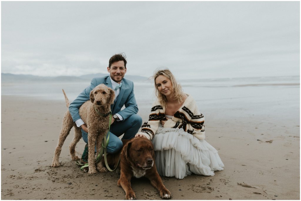 Steve and Holly kneel on the sand with their dogs around them.