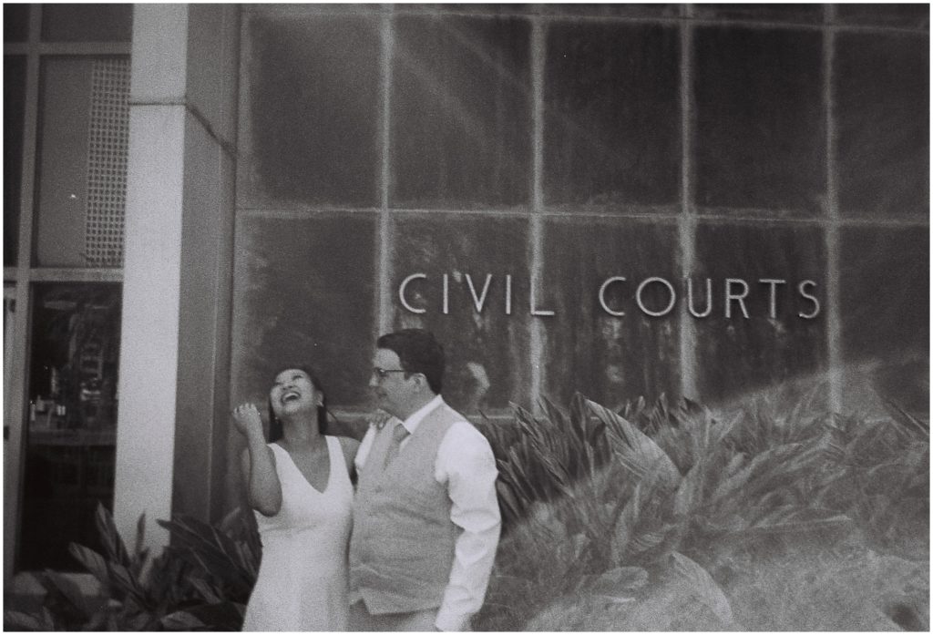 A bride stands beside a groom laughing outside a New Orleans courthouse wedding.