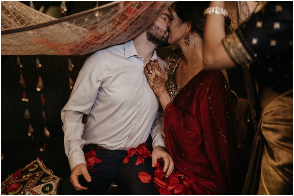 A bride and groom kiss beneath a rose-covered veil at a Posh Puja ceremony at Capulet.
