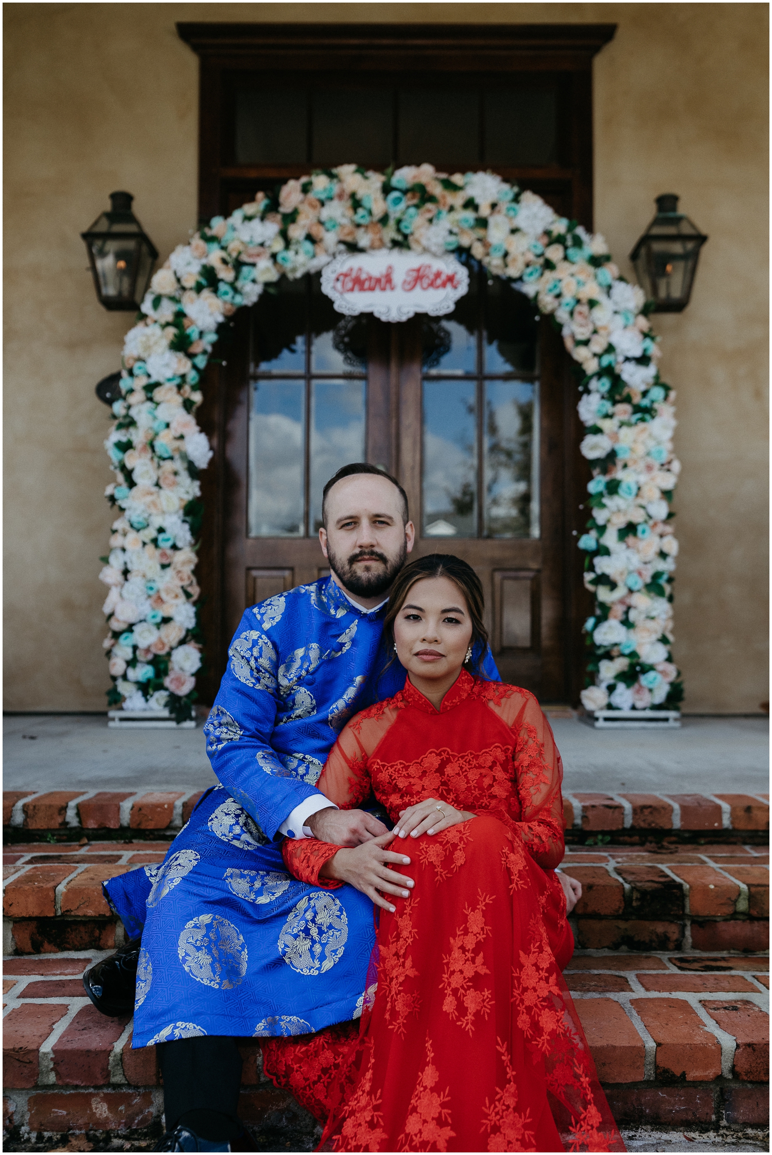 A couple in traditional Vietnamese wedding clothes sit on a porch before an event for their weekend wedding itinerary.