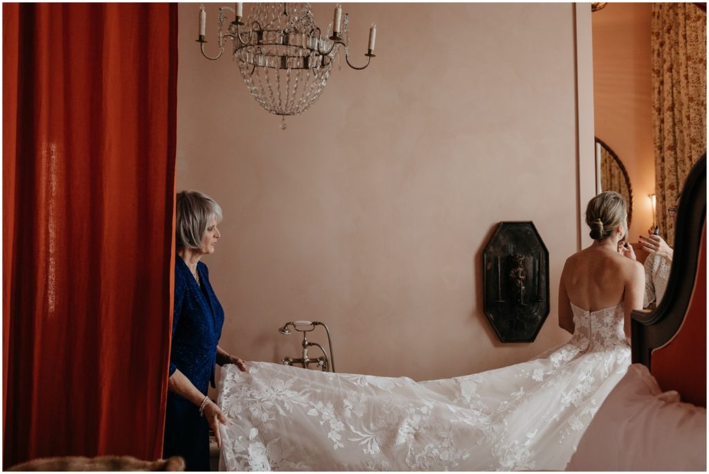 A woman carries the train of a bride's gown as they exit a hotel room.