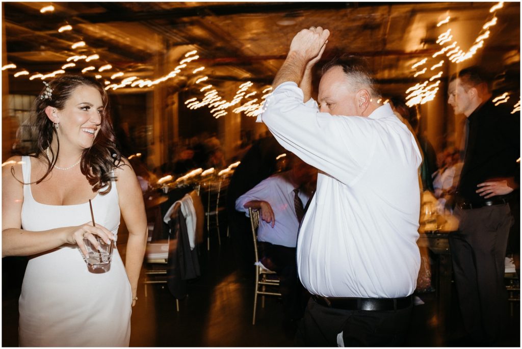 Alex and her father dance with drinks in hand.