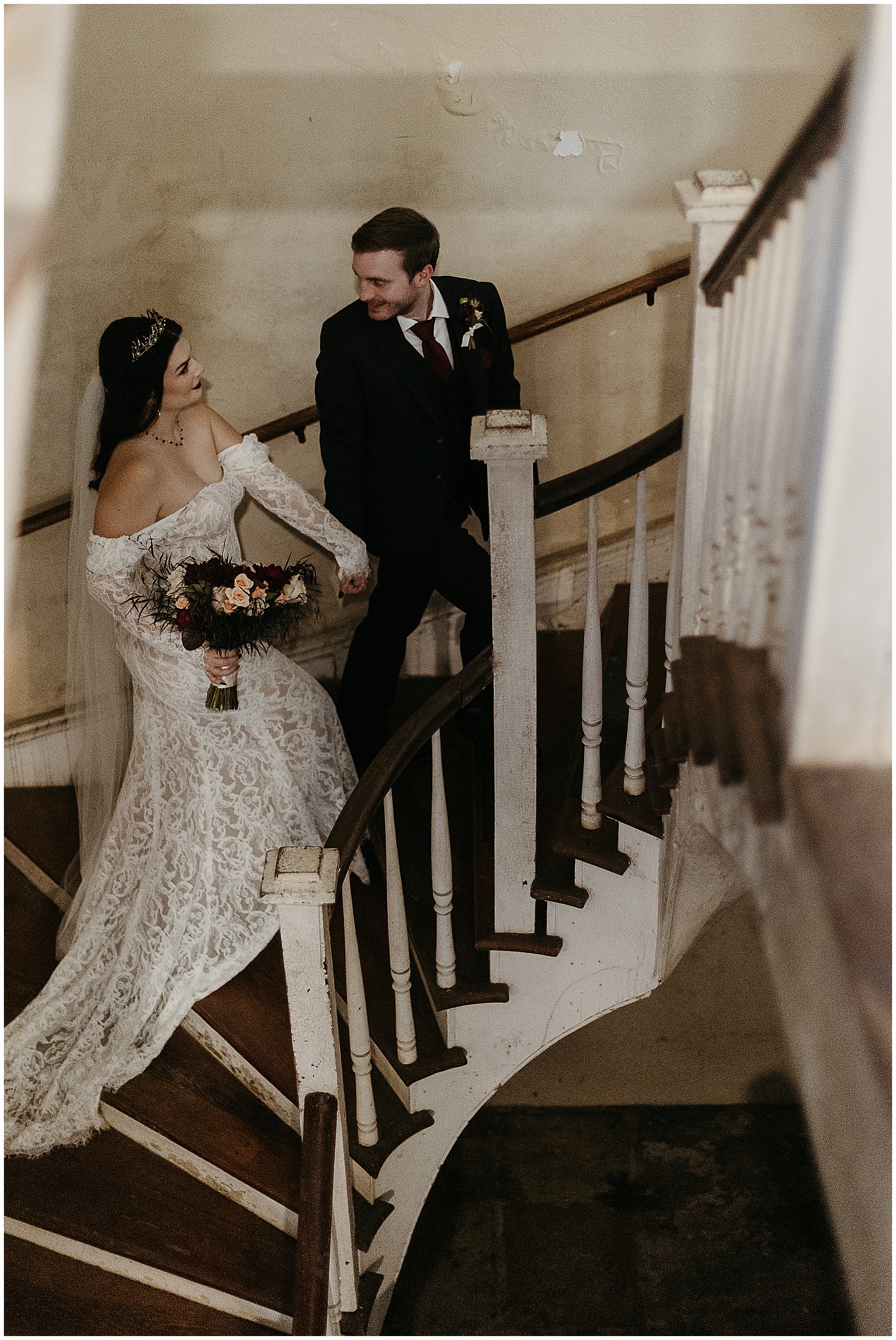A bride and groom walk up an old staircase towards a gothic wedding.