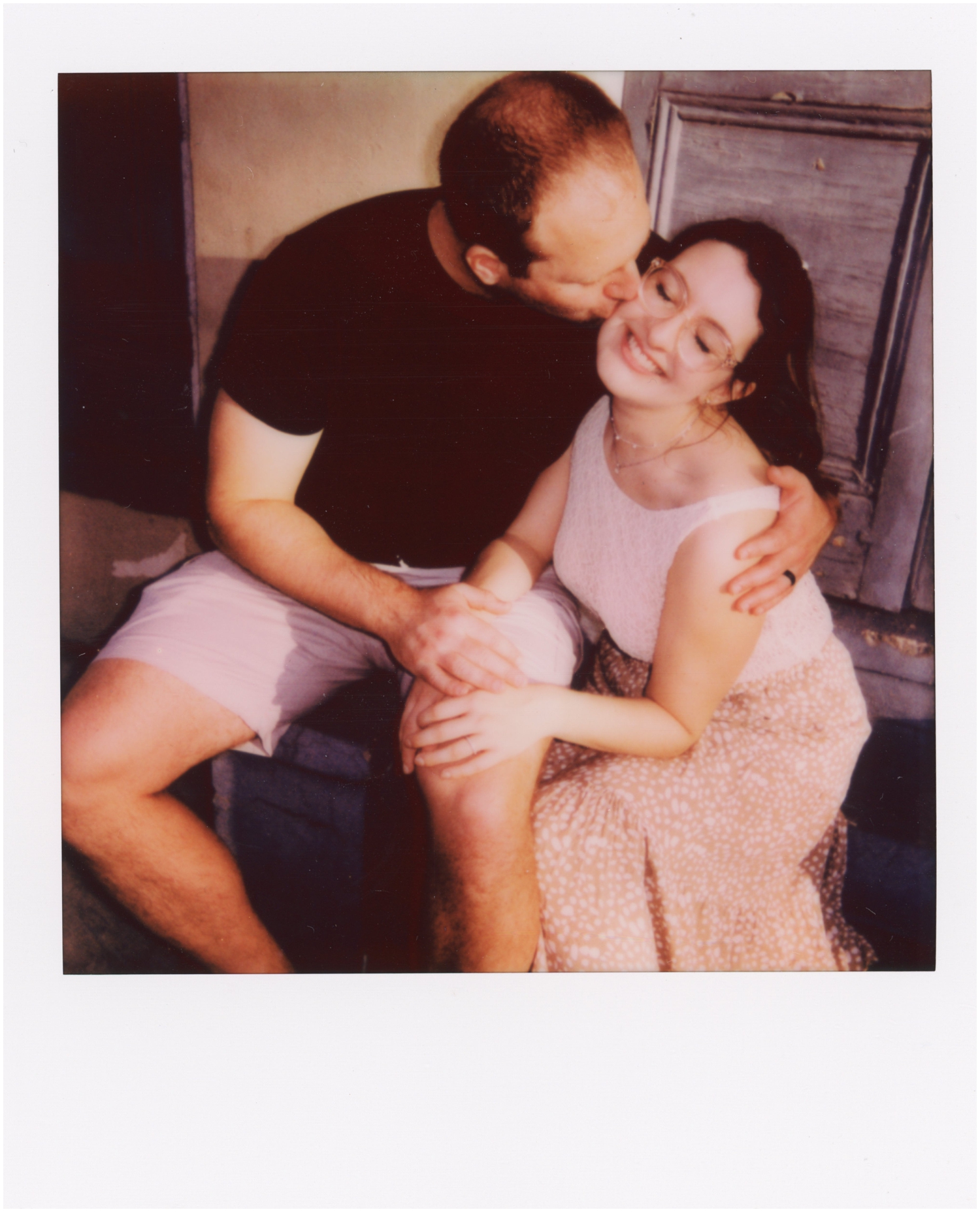 A man and woman sit on a stoop and cuddle during their honeymoon photoshoot.