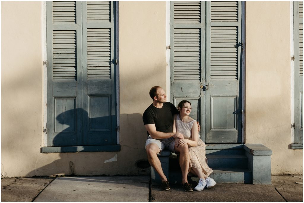 Eric and Lauren sit on the stoop of a yellow French Quarter house in front of blue shutters.