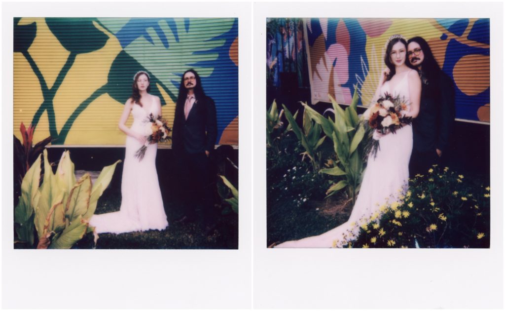 Jared and Penny lean against each other in front of a colorful mural at their winter garden wedding.