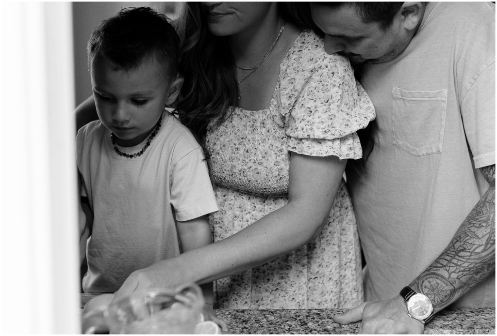 A mother and father stand behind their child and help him make lemonade during an in-home family photo session.