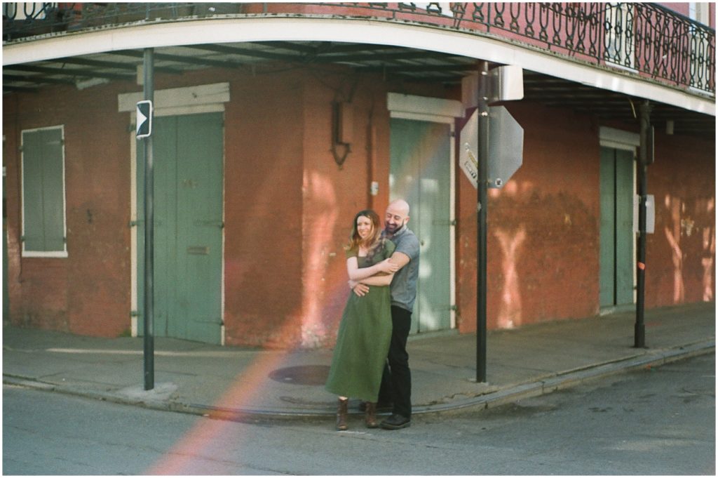 Omar and Anastasia pose in front of an orange and green French Quarter building with a solar flare bisecting the film engagement photo.