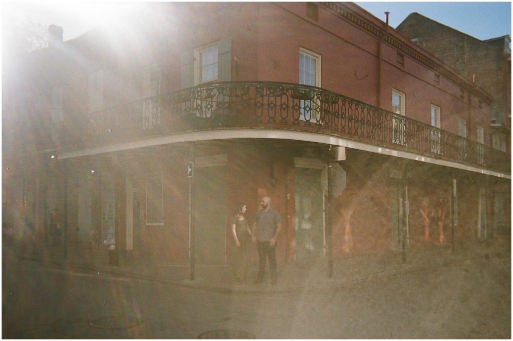 An engaged couple stands under a balcony in New Orleans' French Quarter.