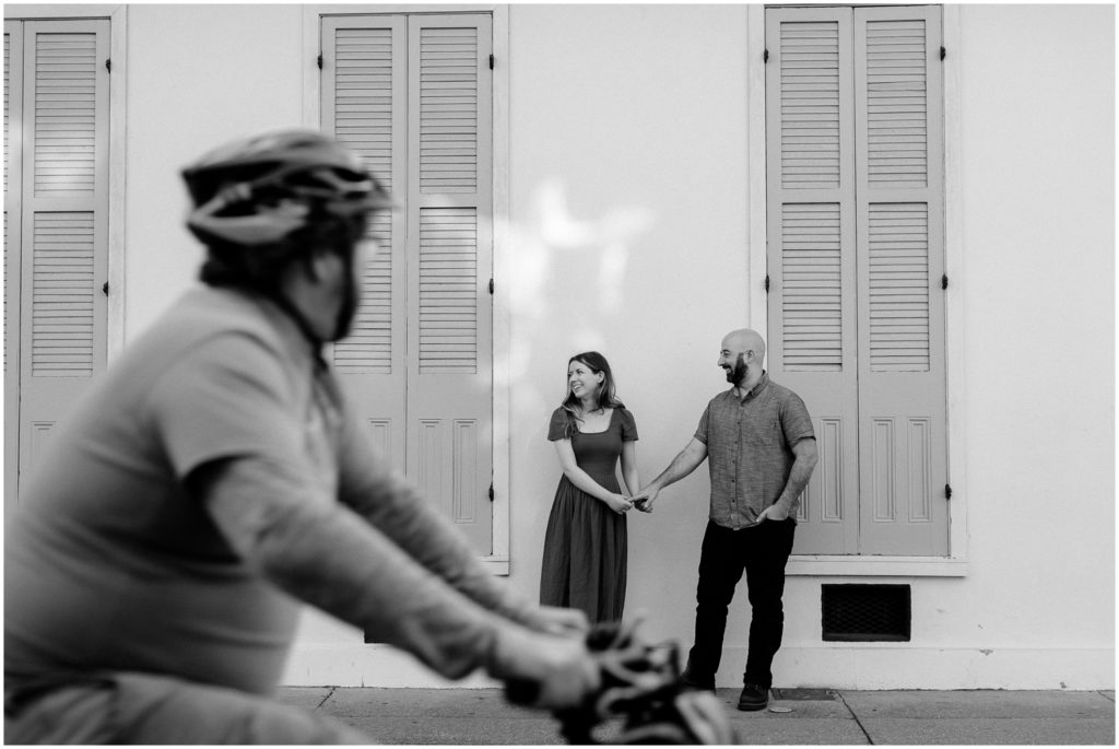 A bicyclist passes a couple on a New Orleans sidewalk during a creative engagement photoshoot.