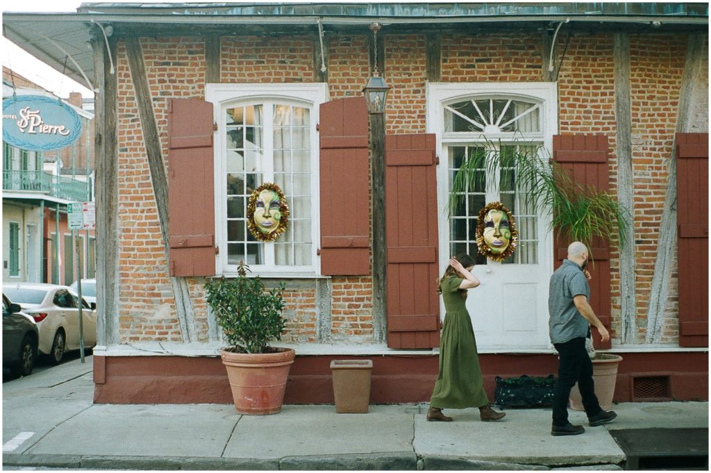 Omar and Anastasia walk past a house decorated with Mardi Gras masks in the windows.