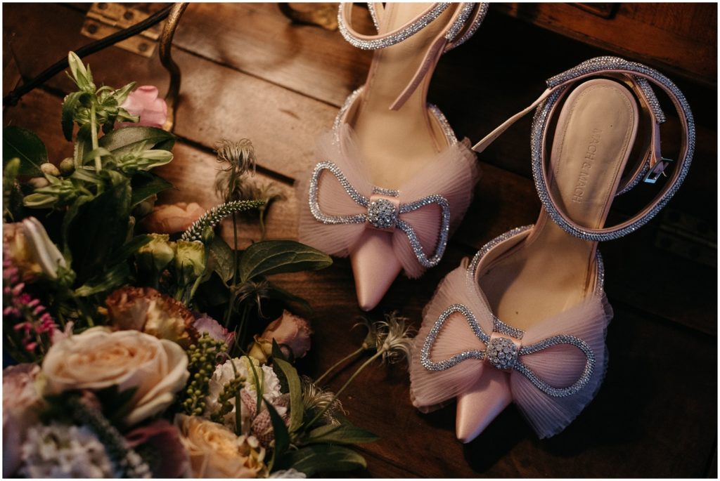 A bridal bouquet lays beside pink wedding shoes.