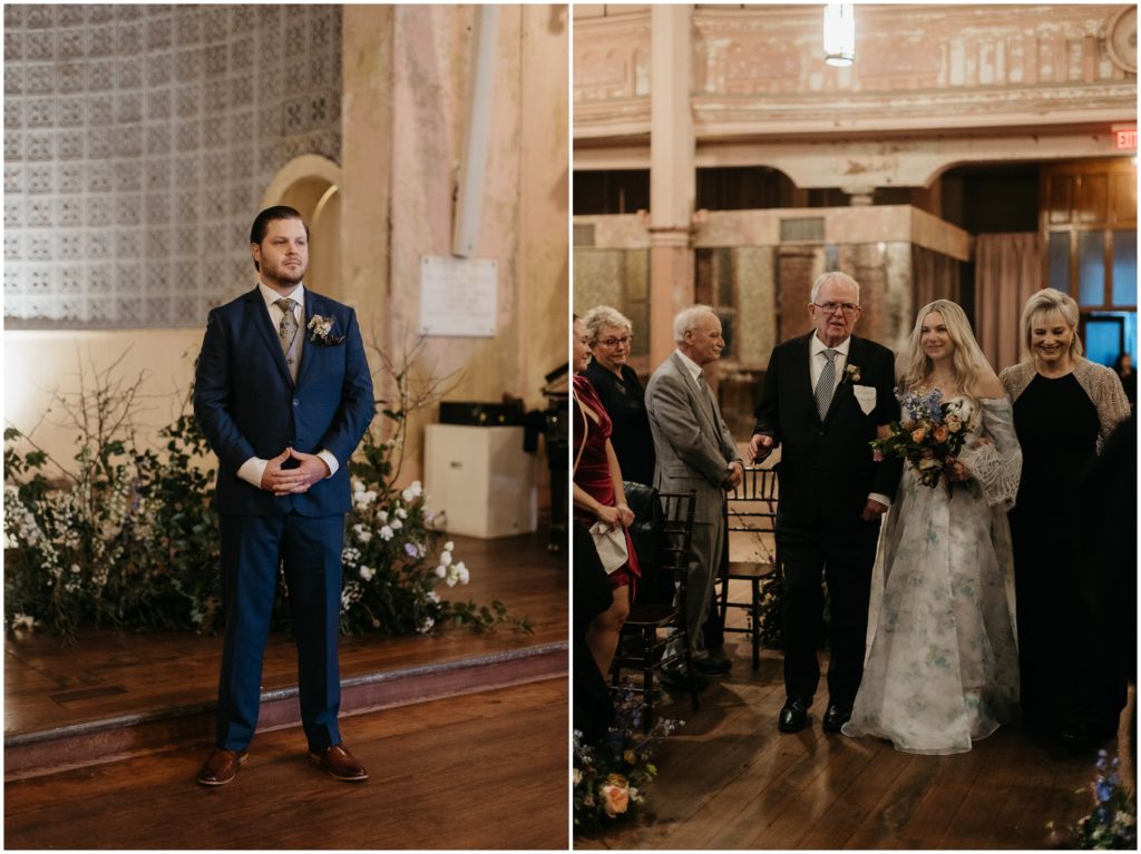 A groom smiles at a bride walking up the aisle in a historic wedding venue.