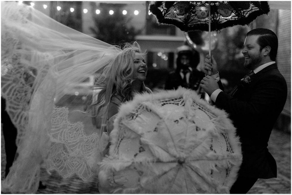 Wind blows a bride's veil and parasol during a New Orleans wedding parade.
