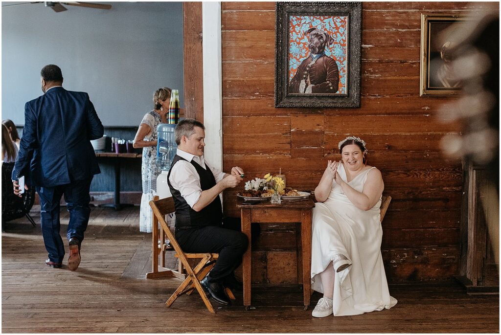 A bride and groom sit in Tigermen Den laughing over a meal.