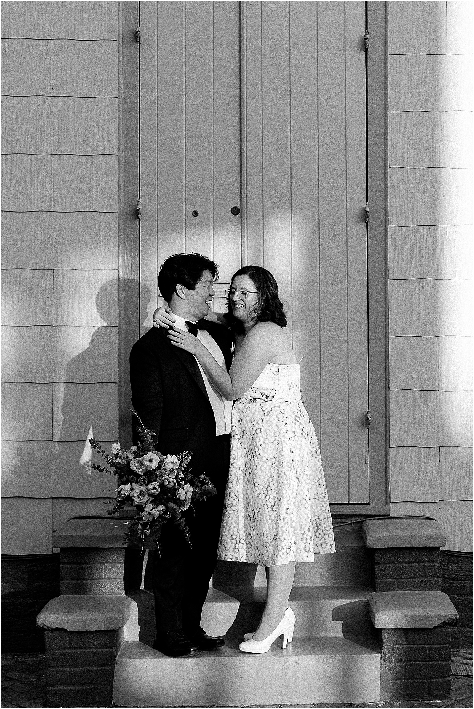 A bride and groom stand in front of a New Orleans house holding a bridal bouquet.