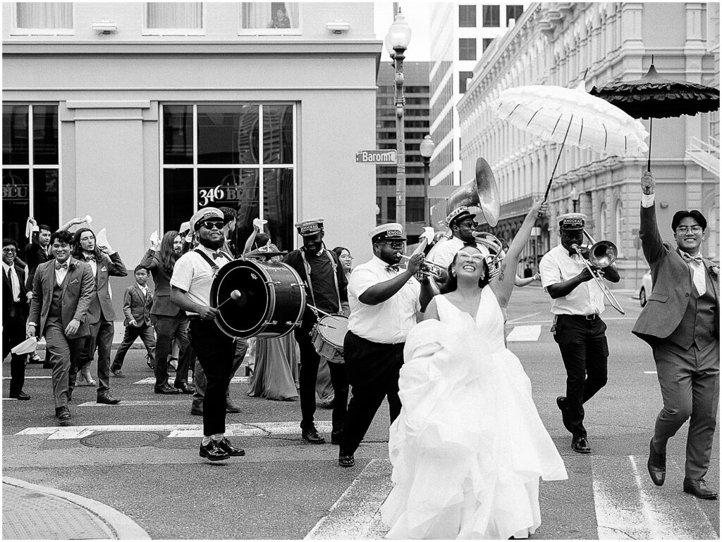 A brass band follow a bride and groom down a New Orleans street.