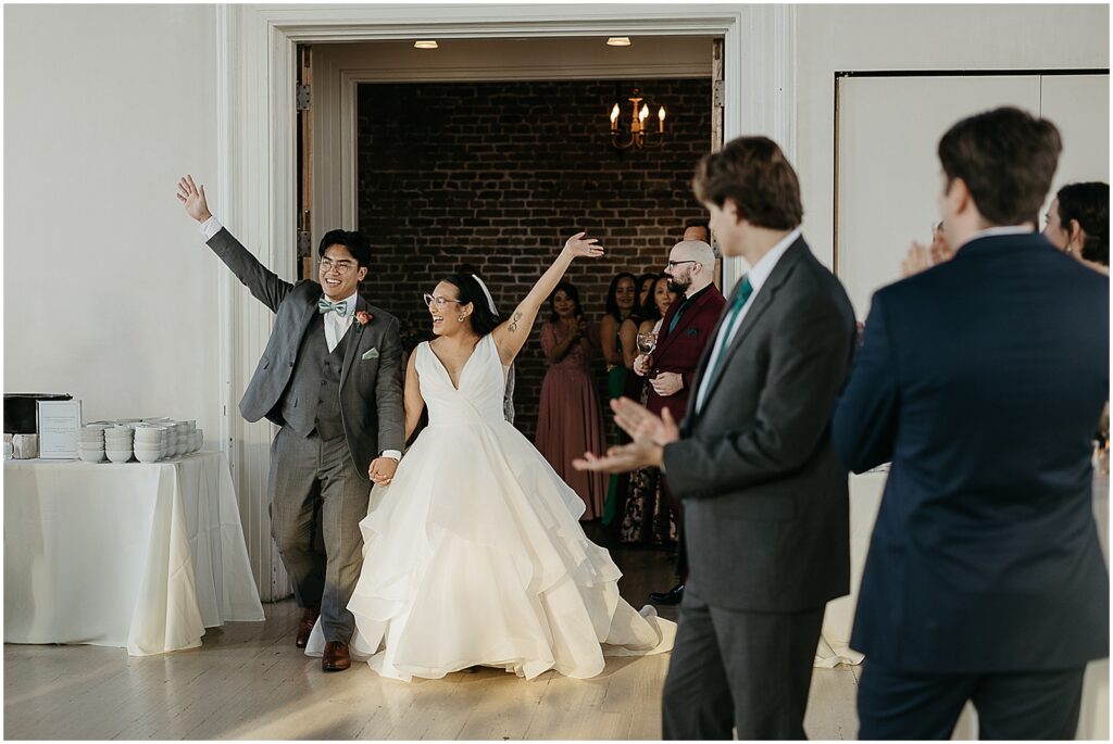 A bride and groom wave their arms as they enter their New Orleans wedding reception.