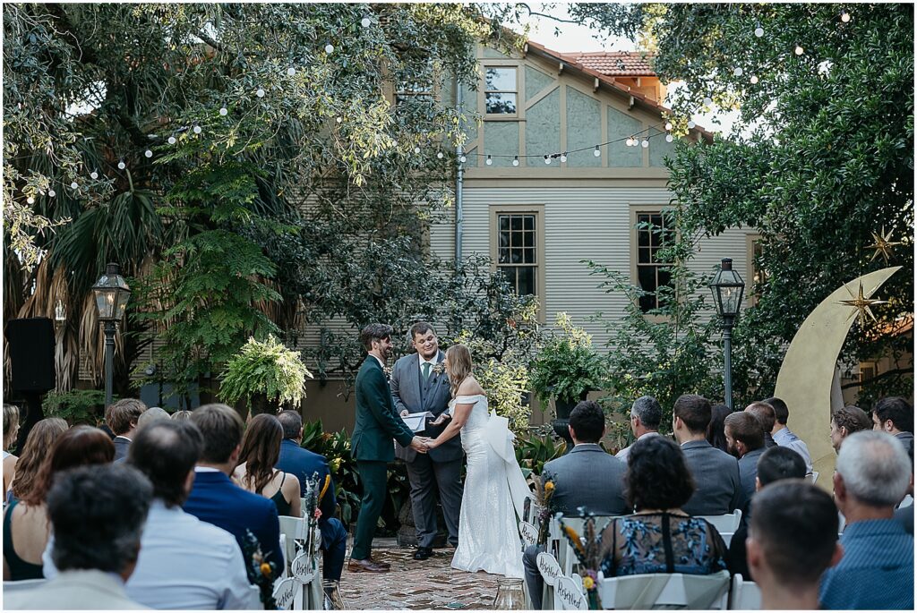 A bride and groom hold hands during a courtyard wedding ceremony in a New Orleans wedding venue.
