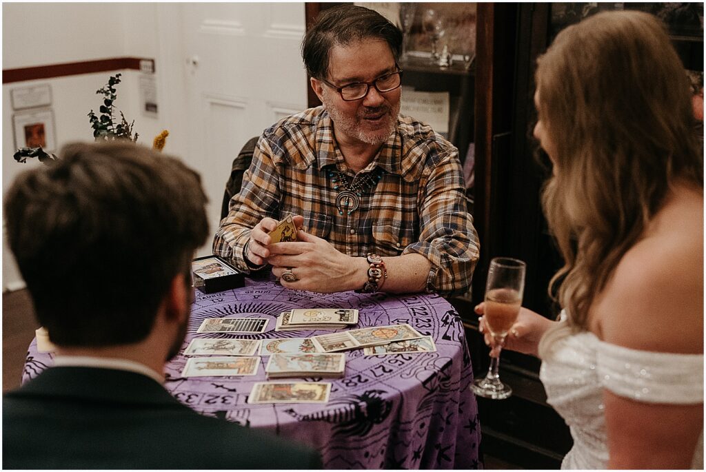 A tarot card reader shuffles a deck while he talks to a bride and groom.