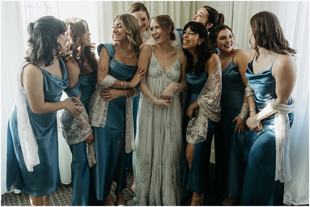 Bridesmaids in blue dresses laugh and crowd around a New Orleans bride.
