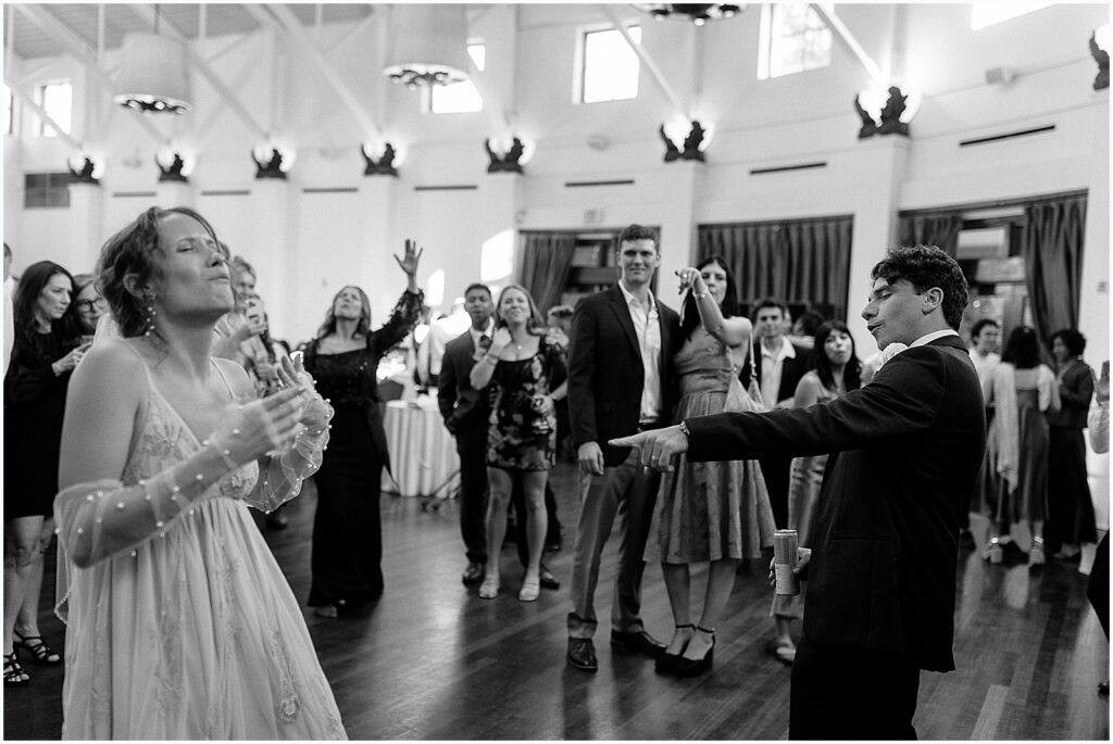 A bride and groom dance with guests at their reception.