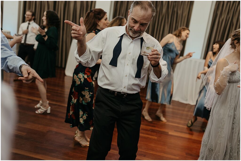 A wedding guest drinks a cocktail and dances.