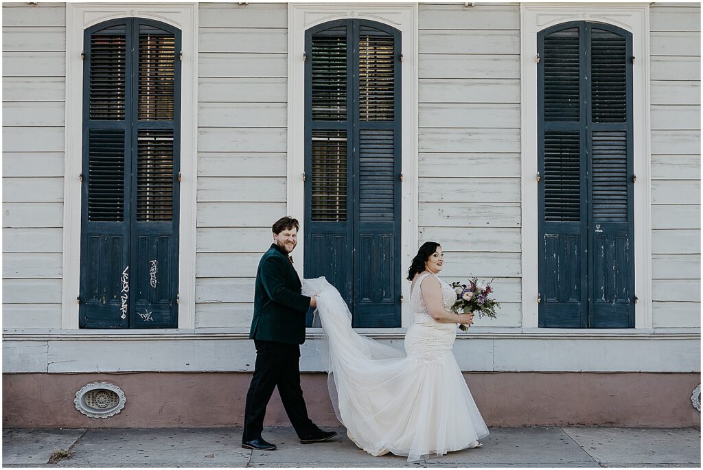A groom carries a bride's wedding dress train down a French Quarter street.