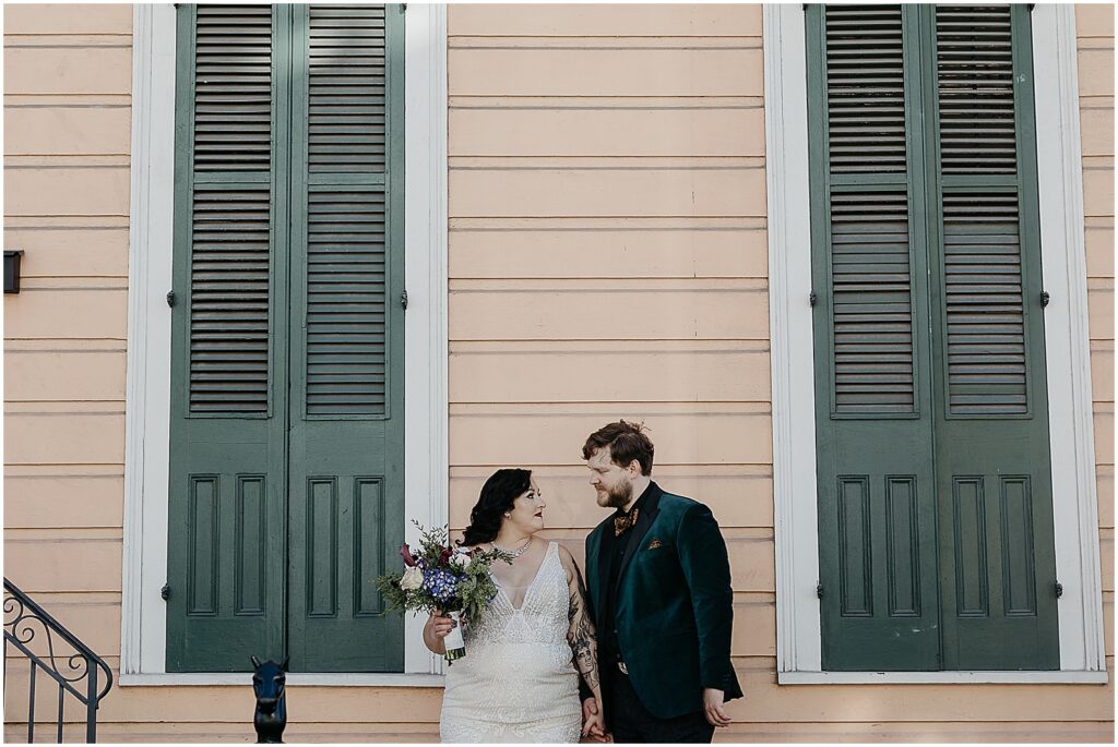 A bride and groom hold hands in front of a French Quarter house.