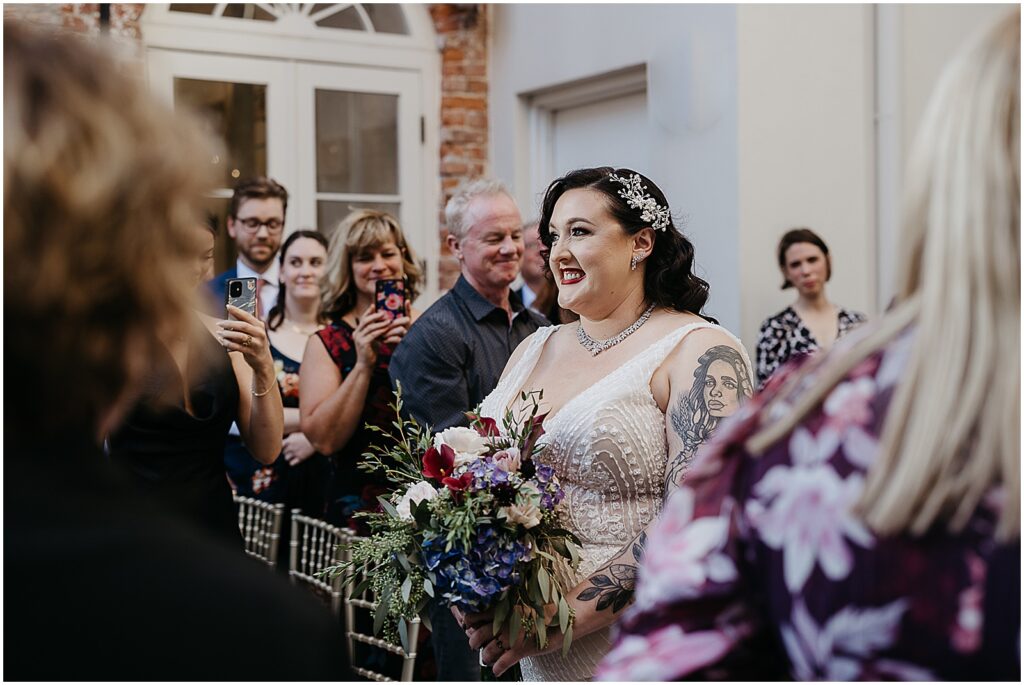 A bride walks down the aisle holding a colorful bridal bouquet.