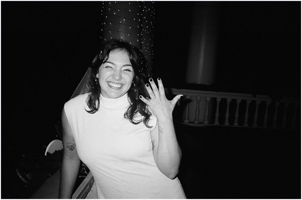 A woman holds up her engagement ring in a black and white engagement photo.