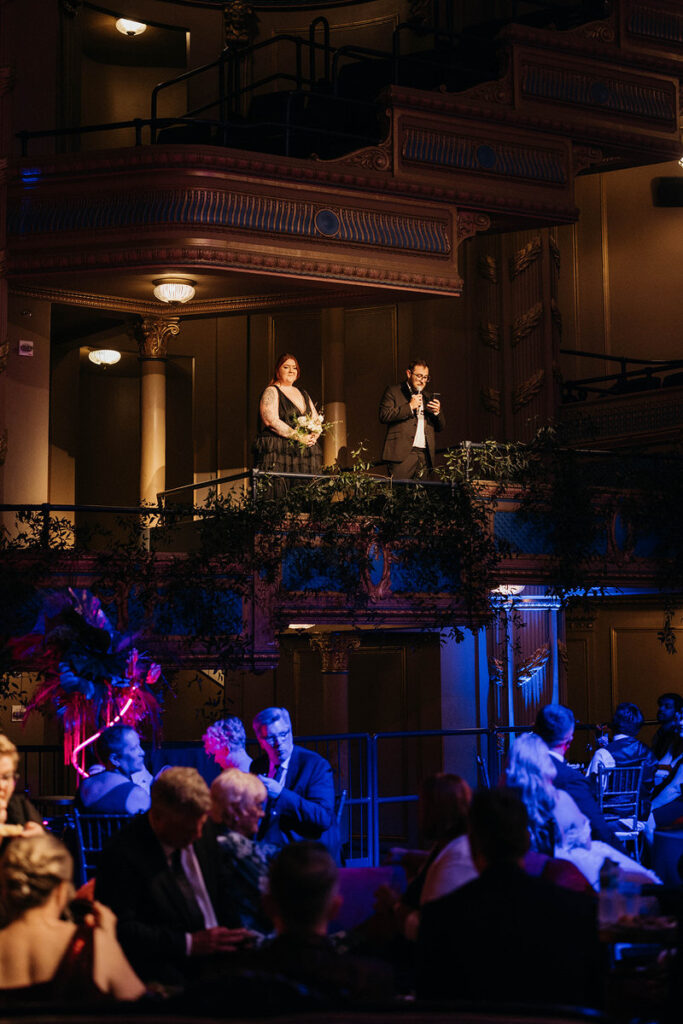 Two people standing in private boxes at an opera theater giving a speech 