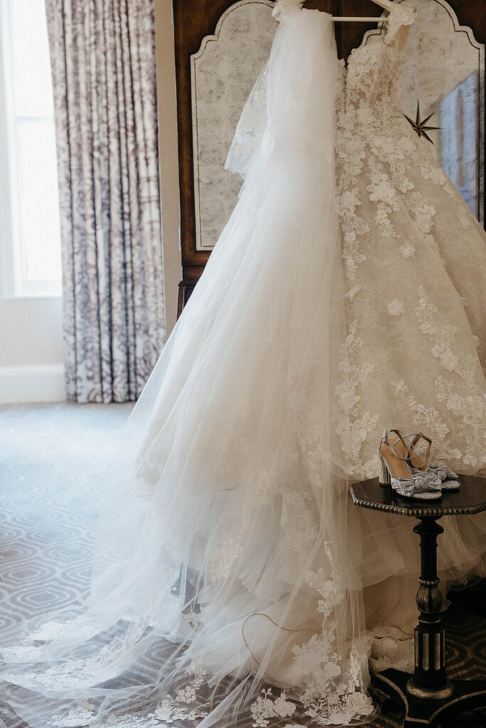 a wedding dress hanging up with heels on a table in front of it. 