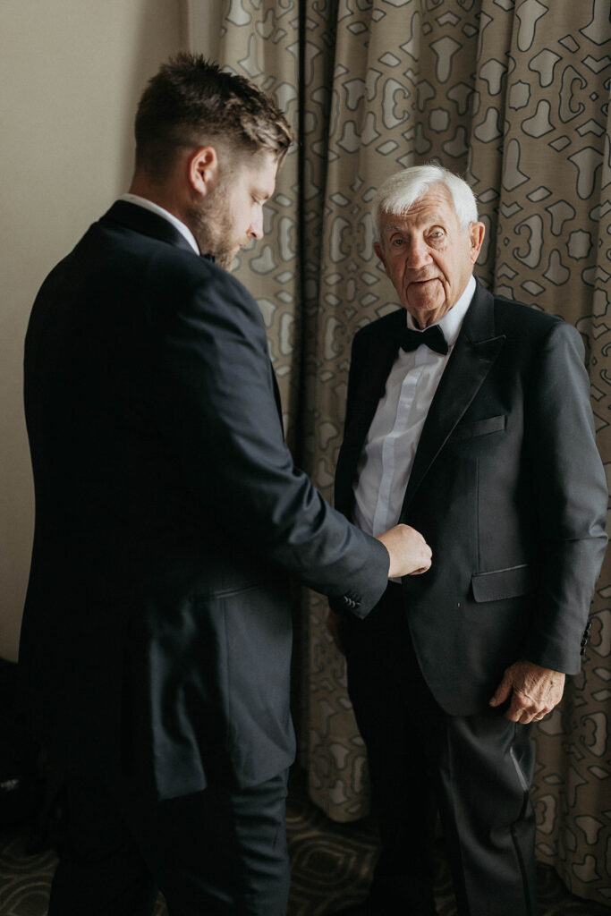 A man helping another man put on a suit jacket 
