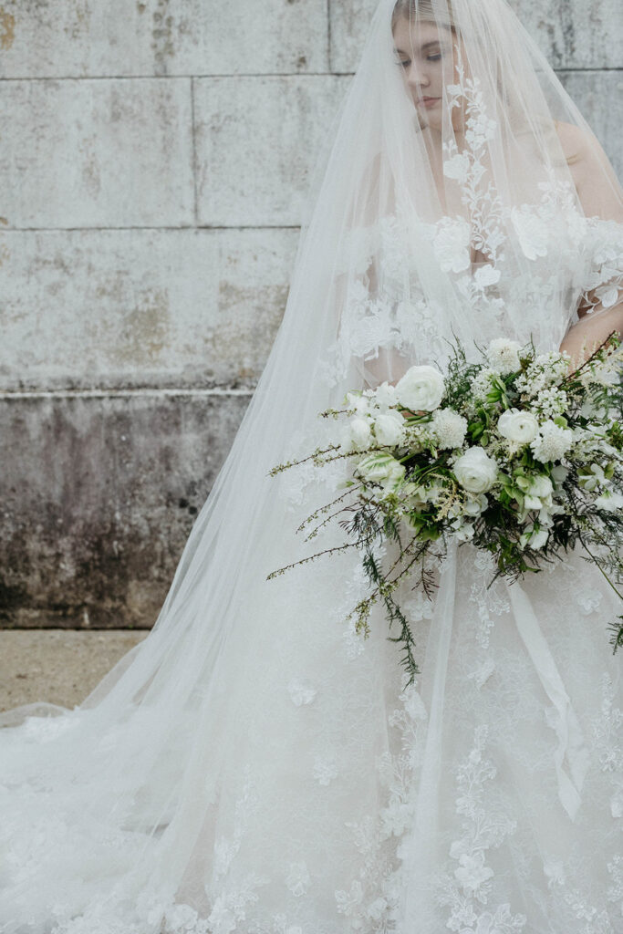 A bride looking down with a veil covering her face while holding a bouquet. 